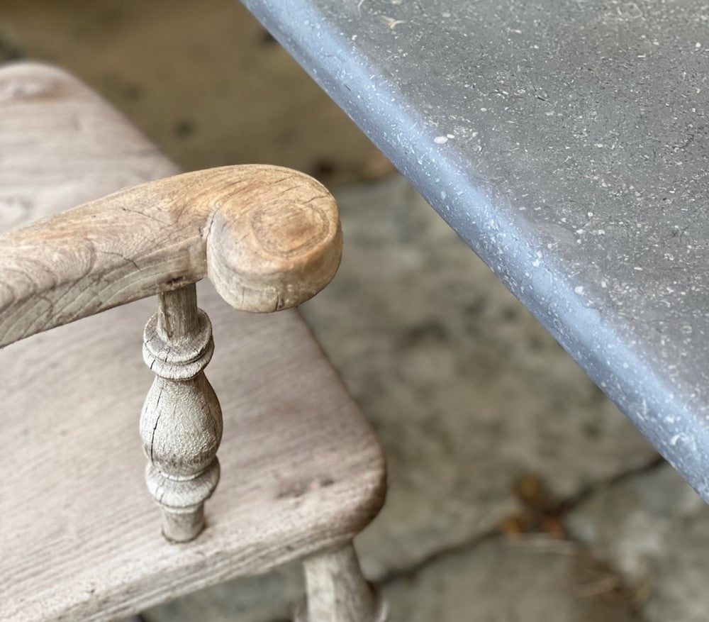 Close-up of a wooden chair armrest and seat with a Belgian blueston surface in the background.