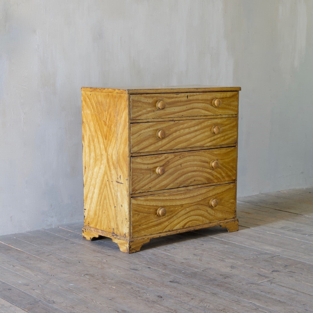 Wooden dresser with three drawers on a wooden floor against a gray wall