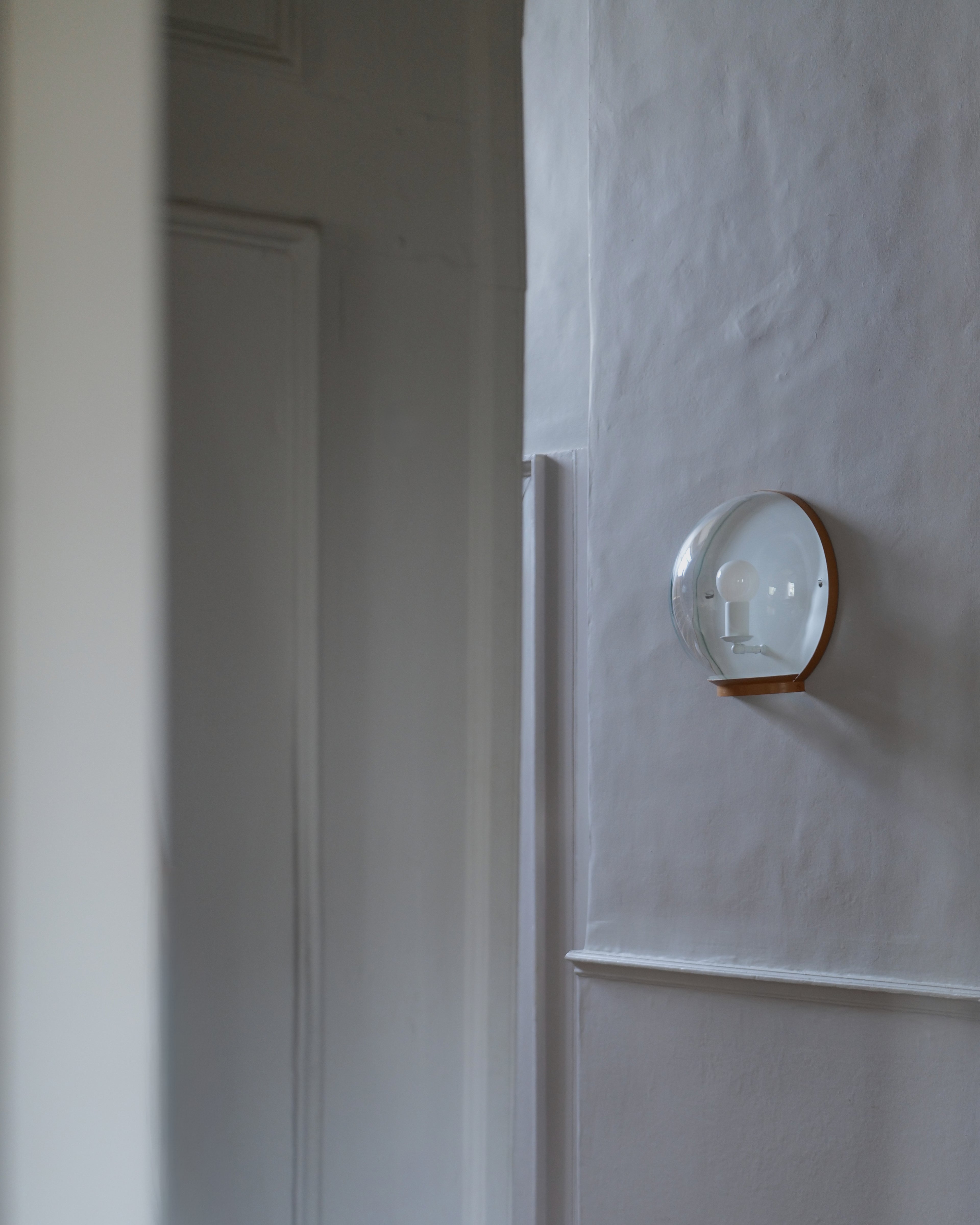 A wall-mounted light fixture with a clear glass dome and a painted metal rim, mounted on a textured grey wall.