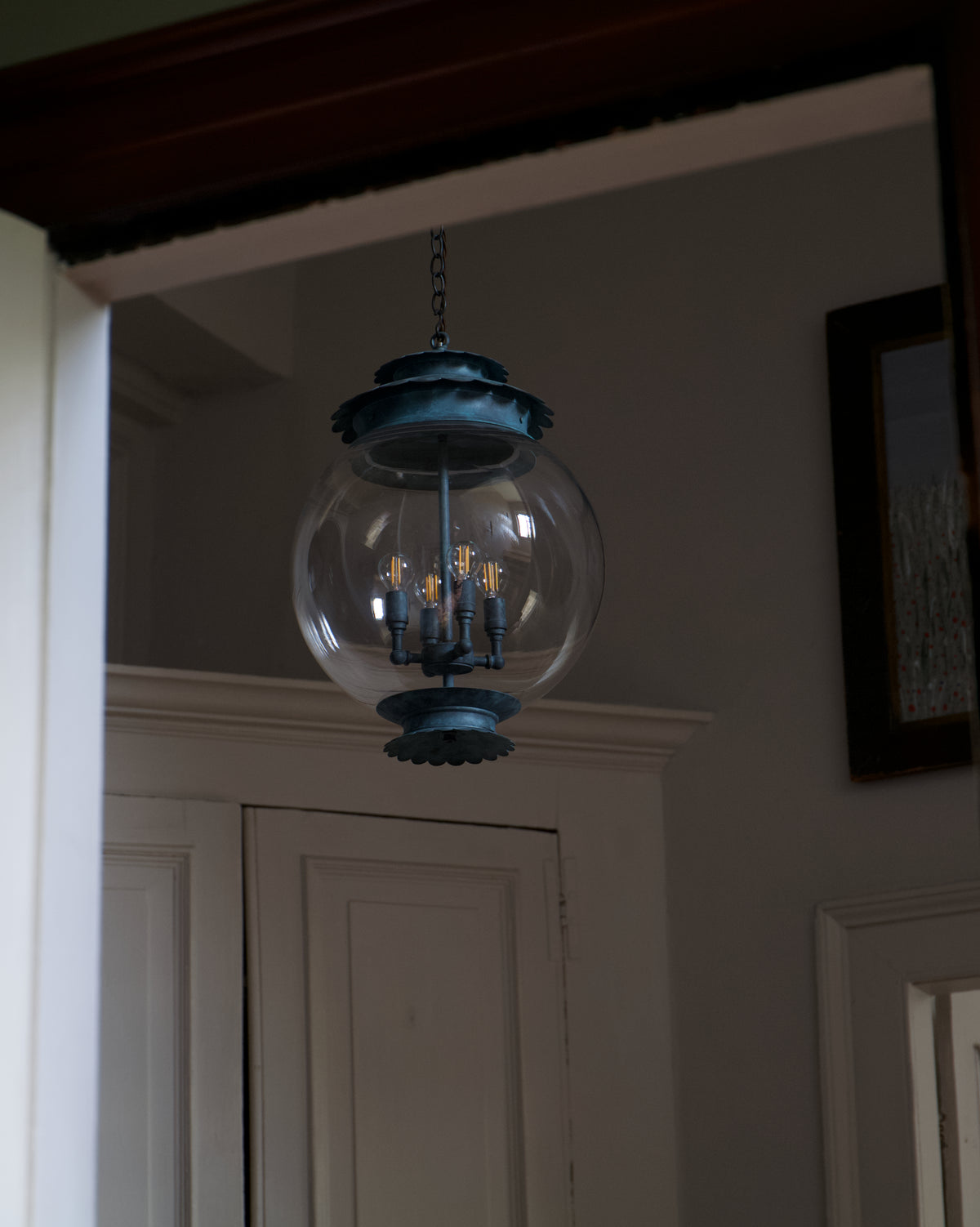A hanging pendant light with a large clear glass globe shade and a dark blue metal frame, suspended in an indoor room with white trim and a dark wood ceiling.