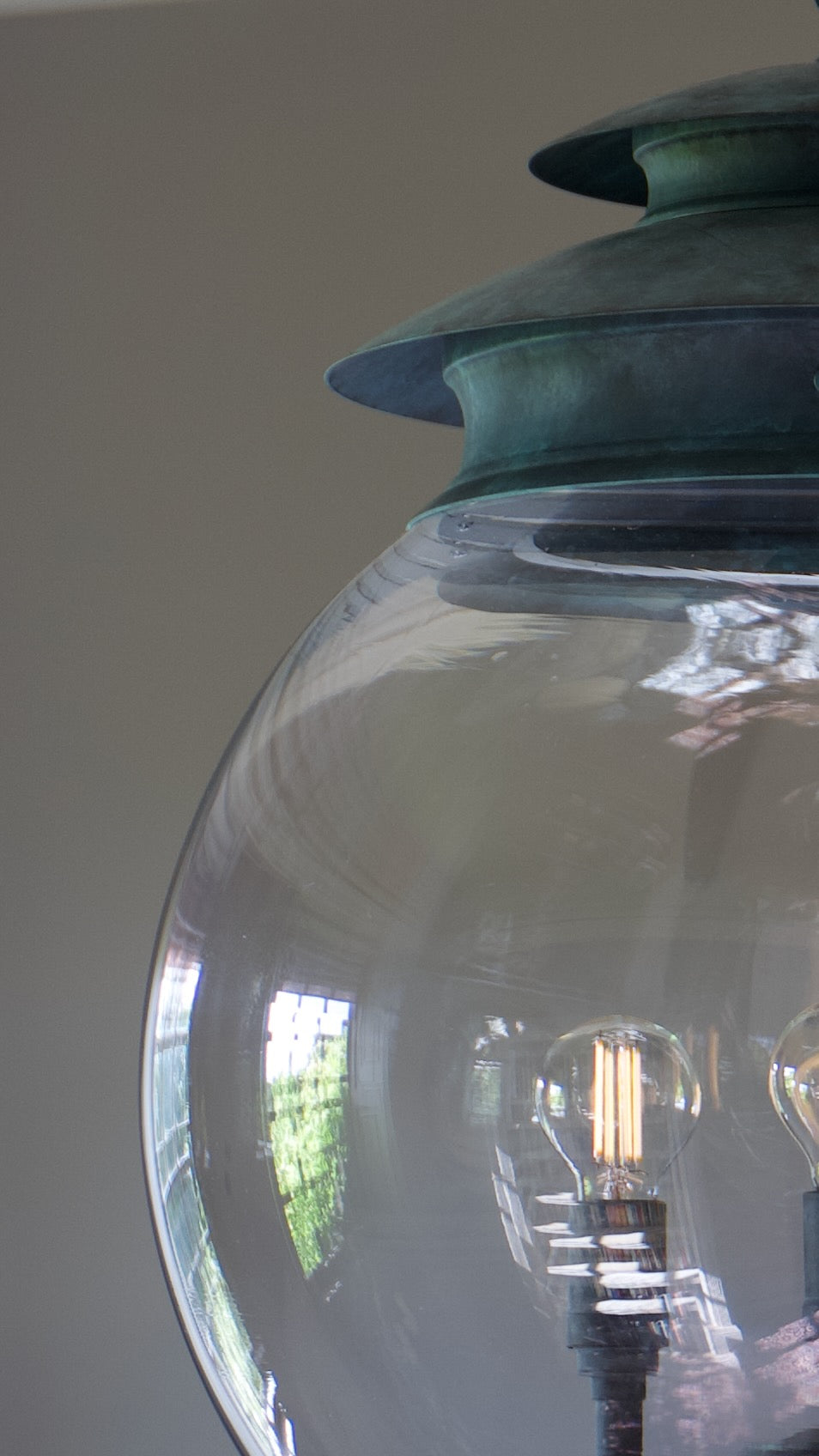 Close-up of a decorative light fixture with a large clear glass globe shade and a layered verdigris brass top, showing an exposed filament bulb inside.