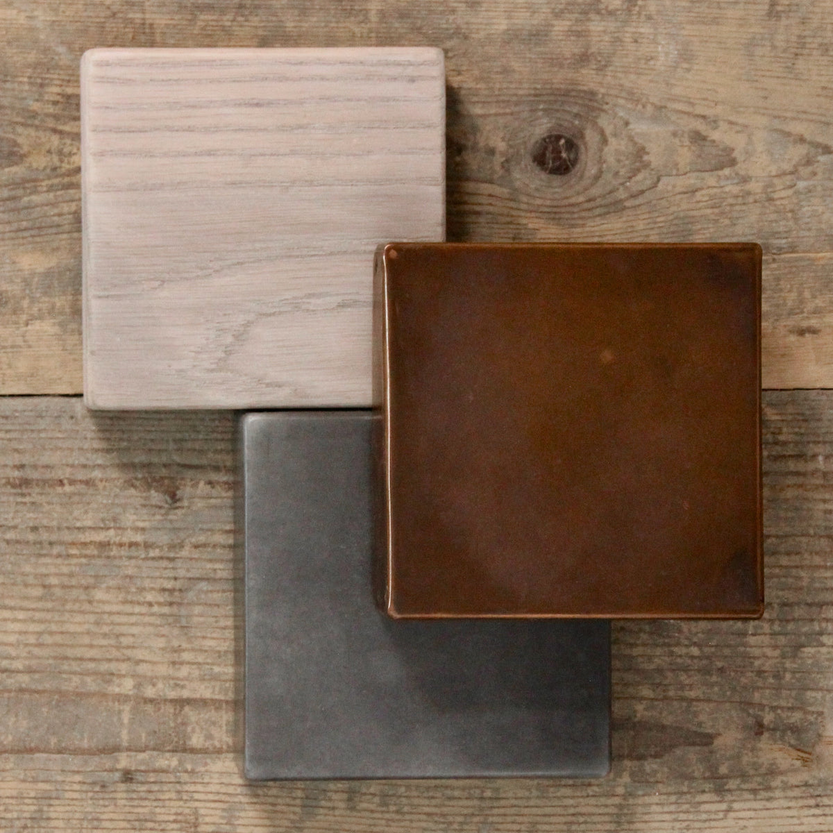 Three square finish samples in oak, copper and zinc, arranged on a rustic wooden table.