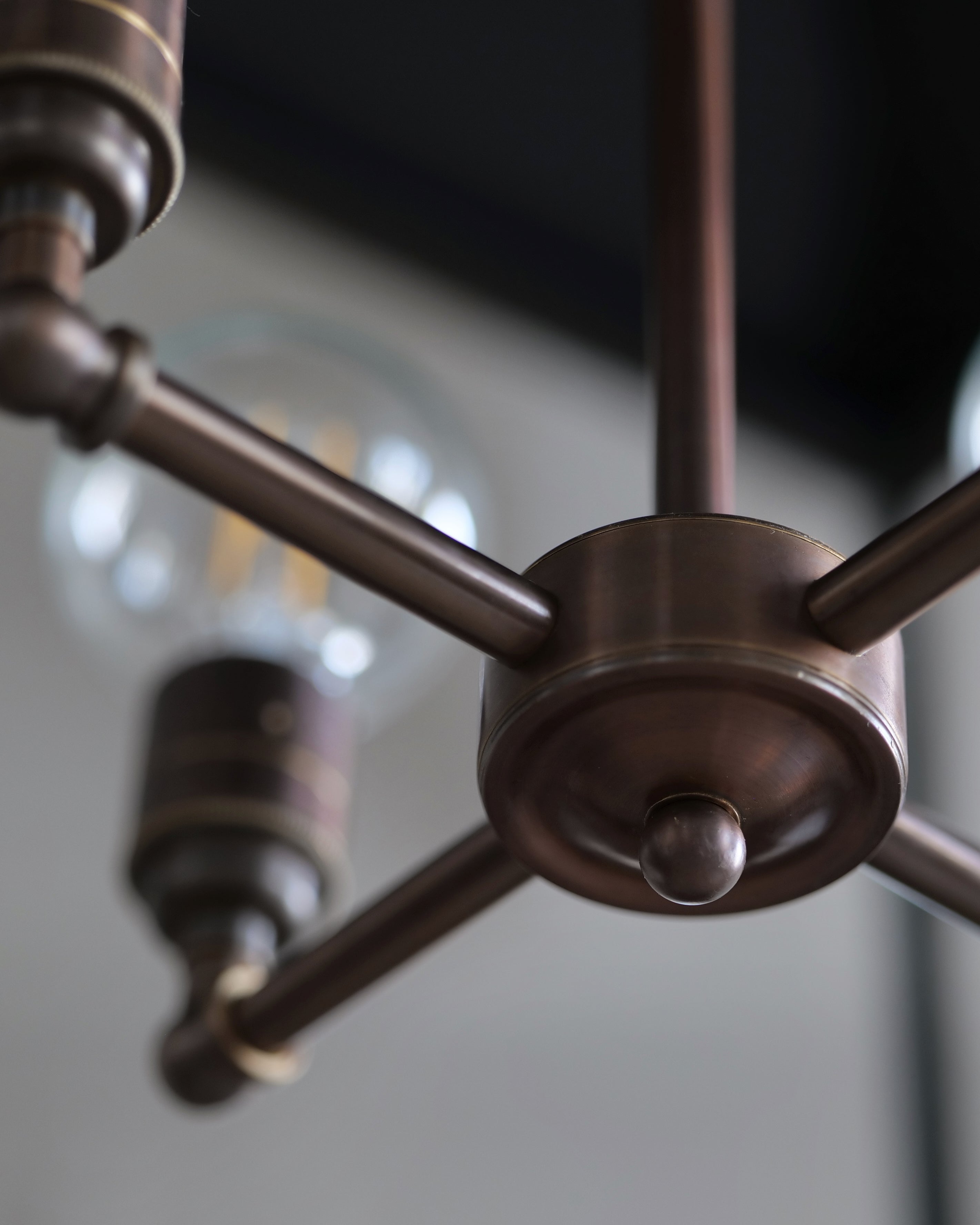 A close-up detail image of the 4-way centre of a lantern made from a dark finished brass and clear glass.