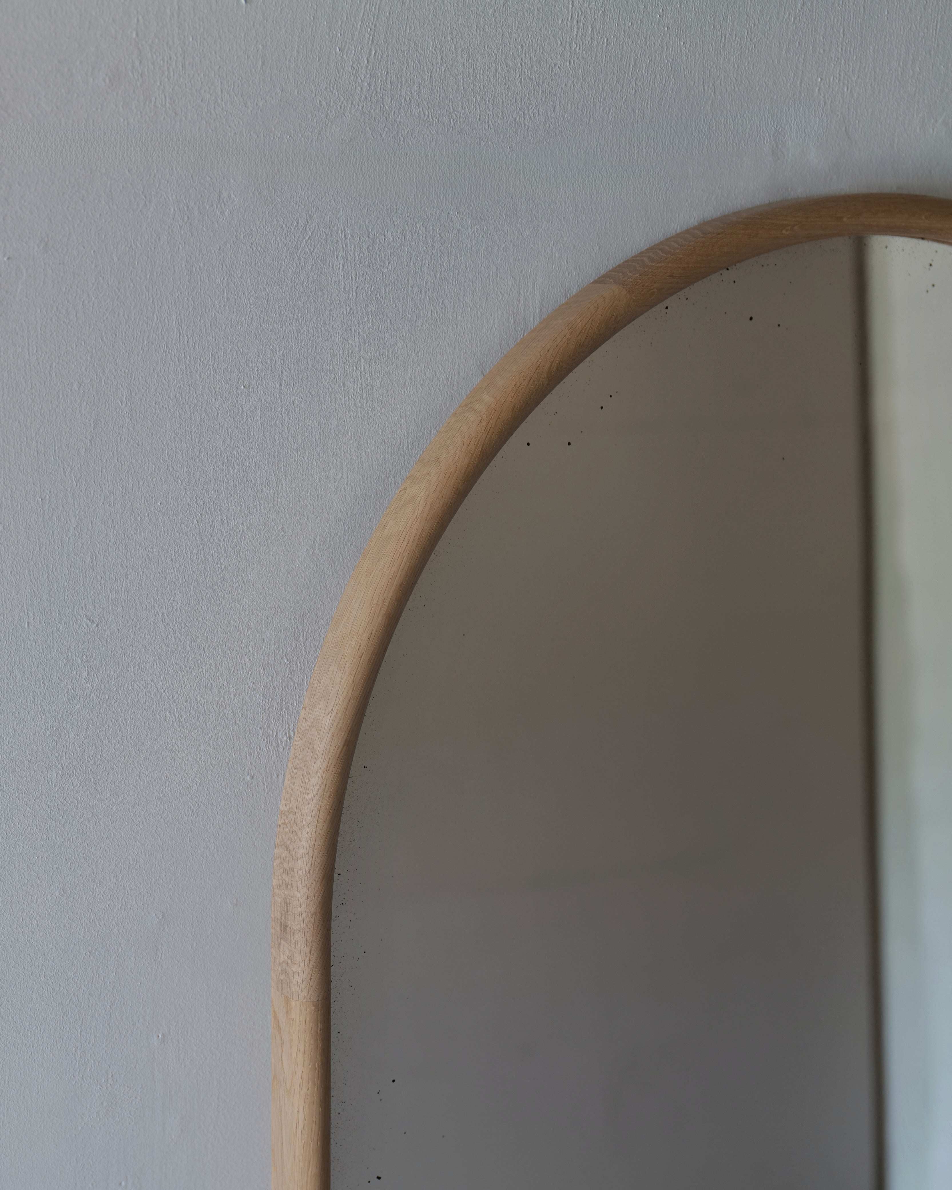 Close-up of an arched wall mirror with a light natural wood frame against a textured off-white wall.