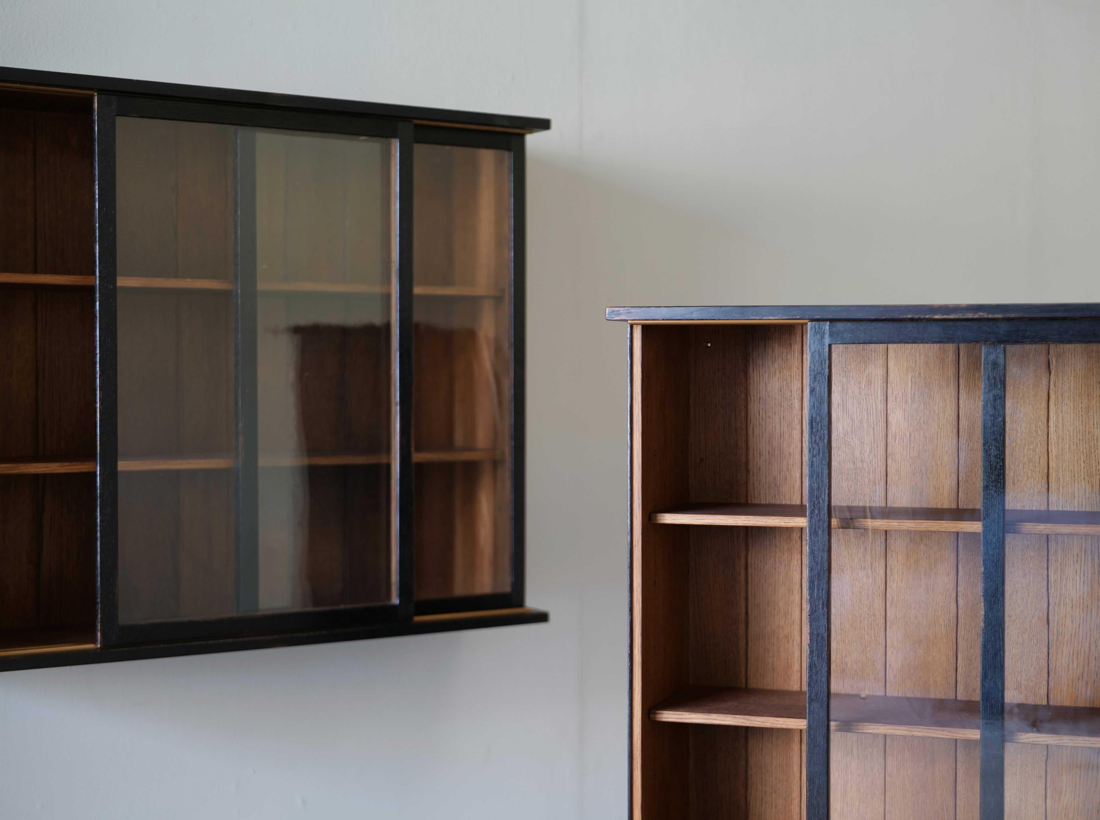 Two oak konami cabinets with black metal frames and cylinder glass doors, shown against a plain off-white wall.