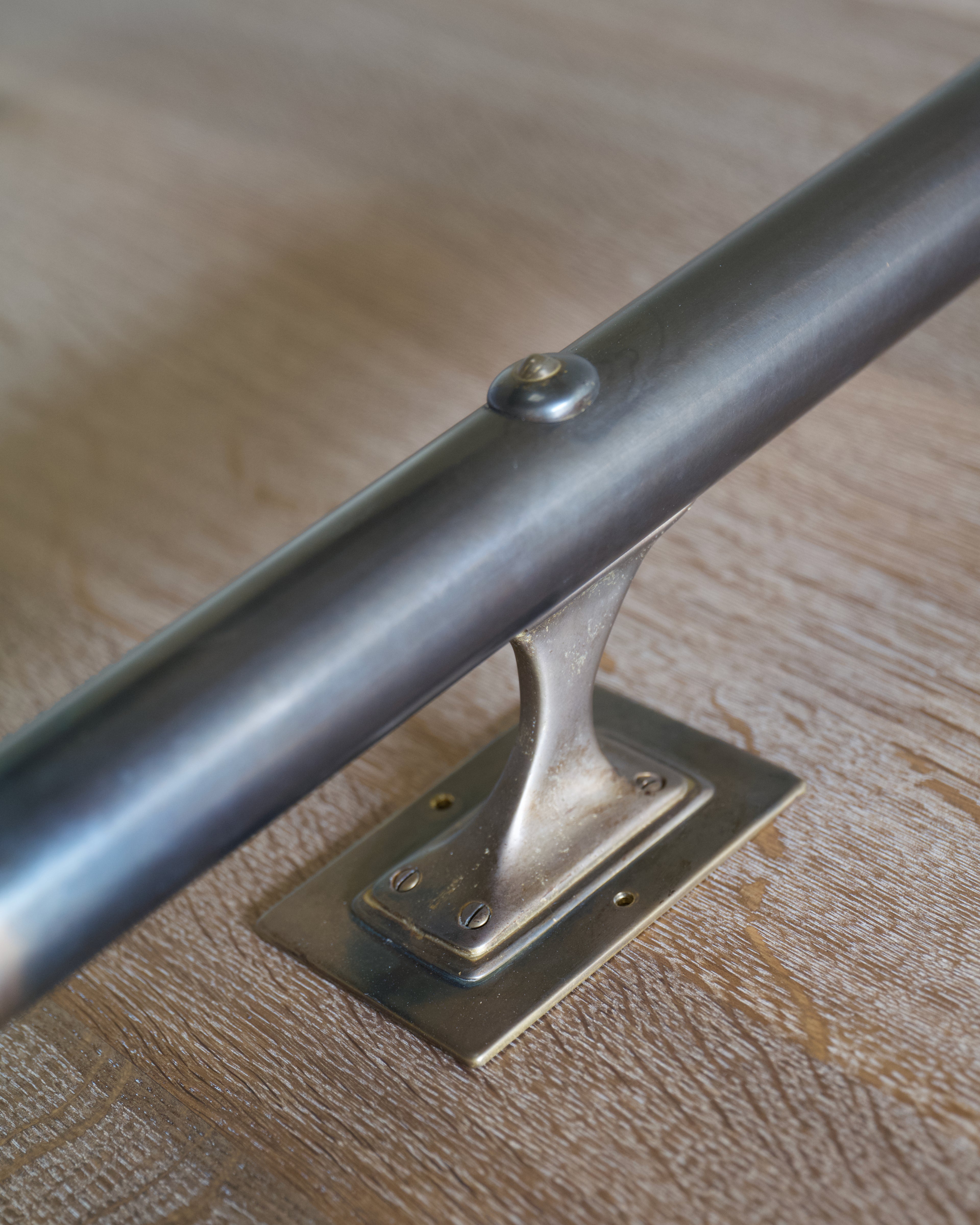A close-up of a dark brass lighting fixture on a light timber surface with a brass wall bracket.