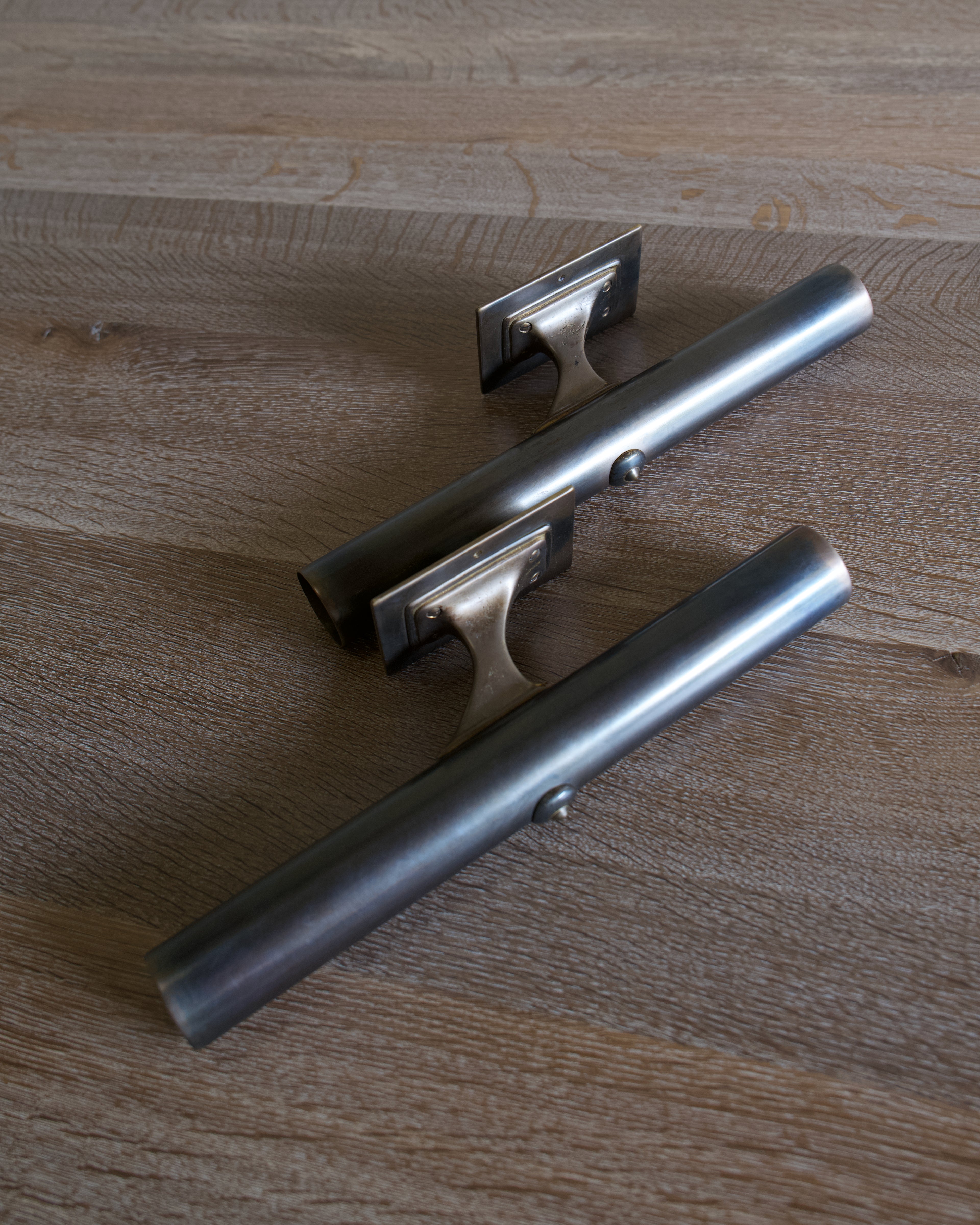 Two cylindrical dark brass lighting fixtures with mounting plates, shown on a light timber surface.