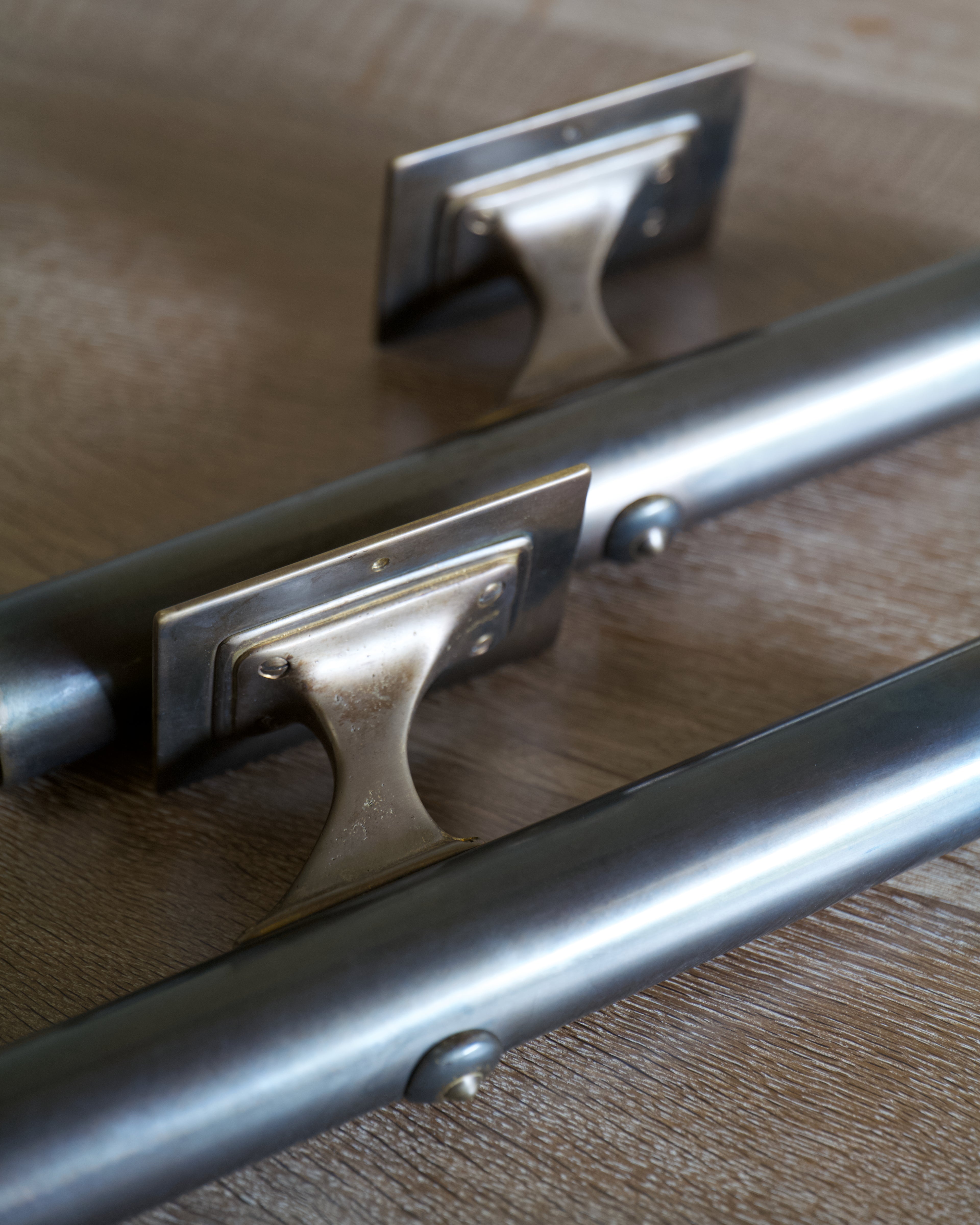 Two cylindrical dark brass lighting fixtures with mounting plates, shown on a light timber surface.