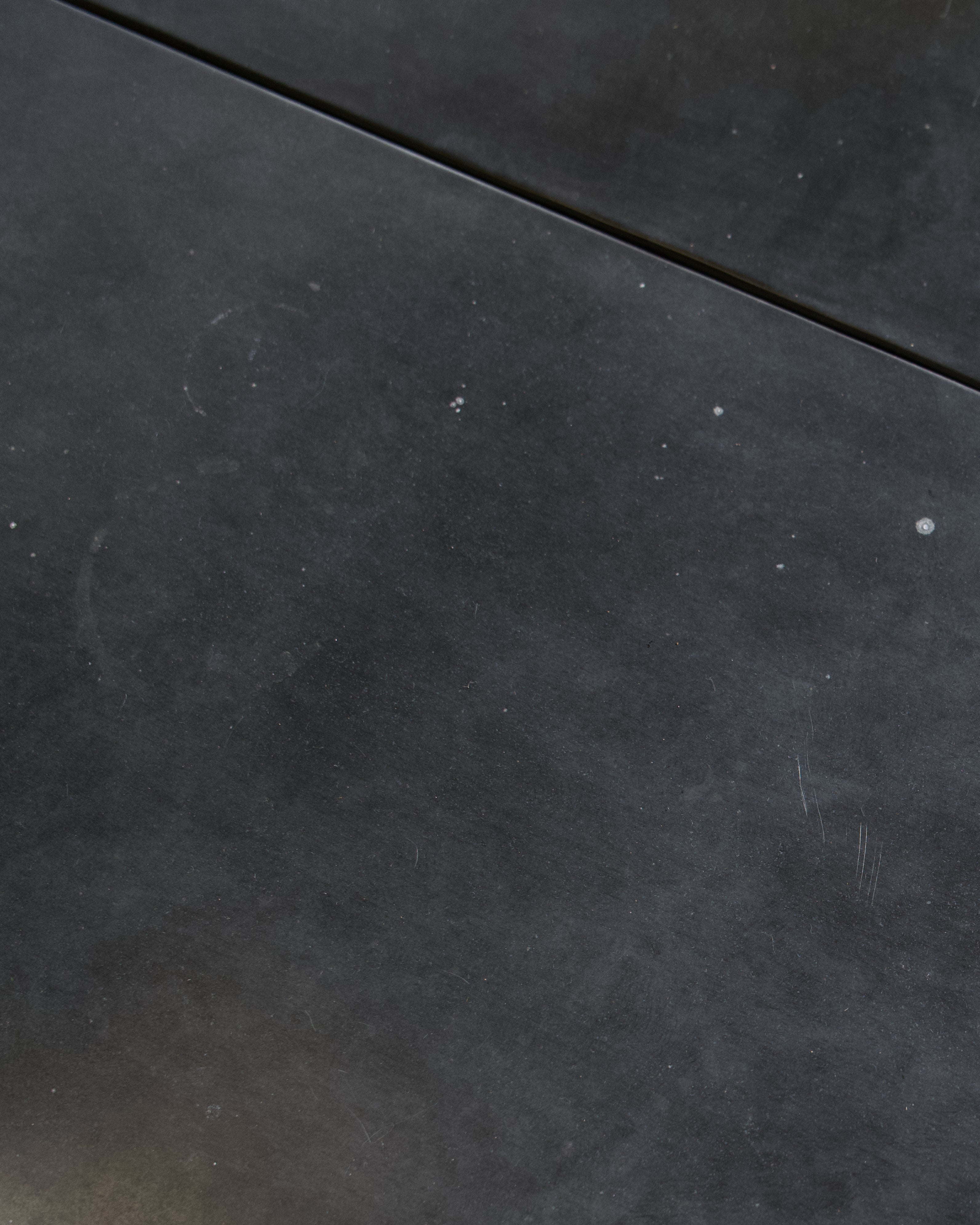 A close-up of a dark zinc surface, with a thin seam visible in the upper portion.