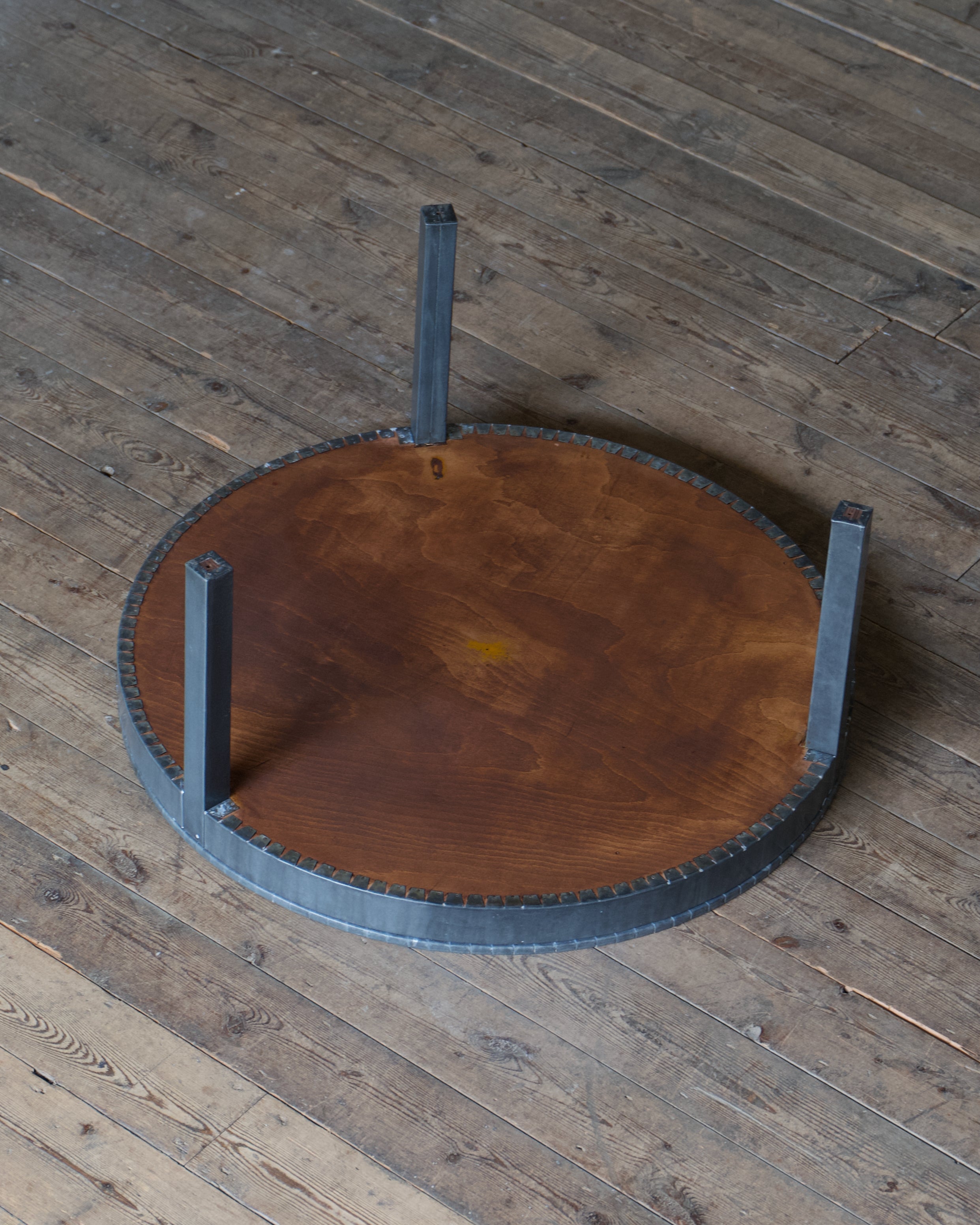 The underside of a circular table wrapped in zinc, set on a wood floor.