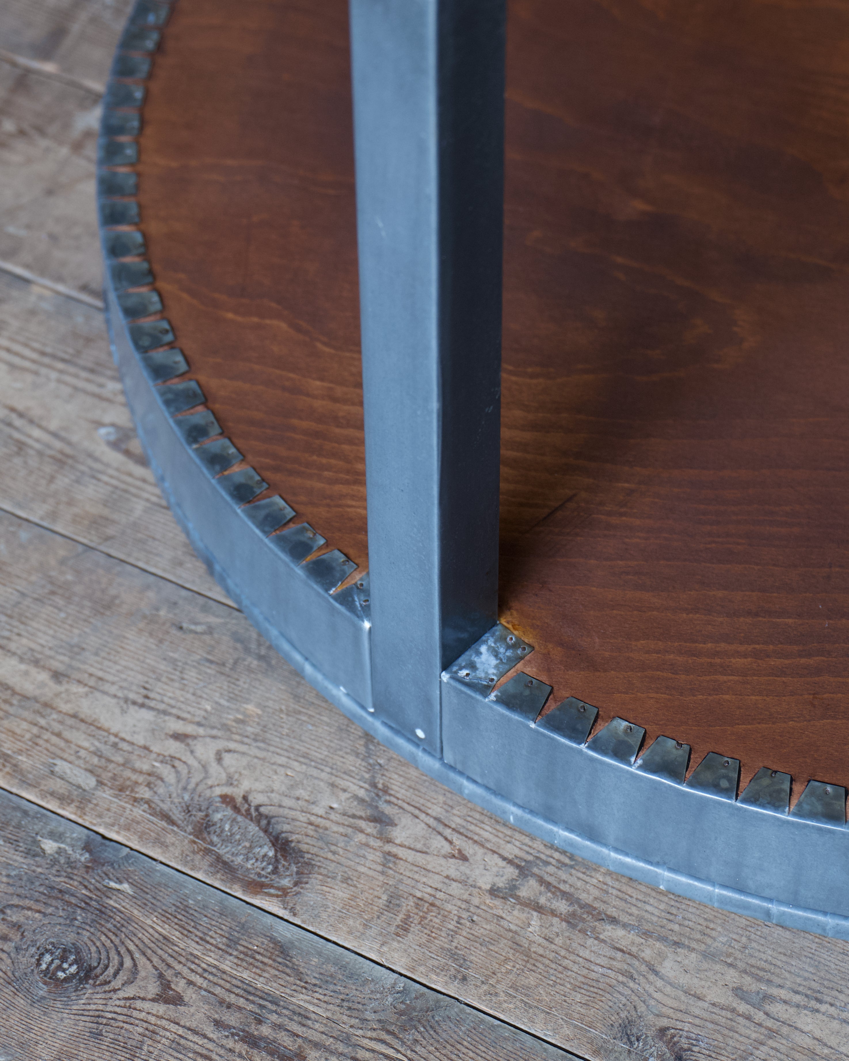 A close up of the underside of a zinc wrap on a circular timber table, set on a wooden floor