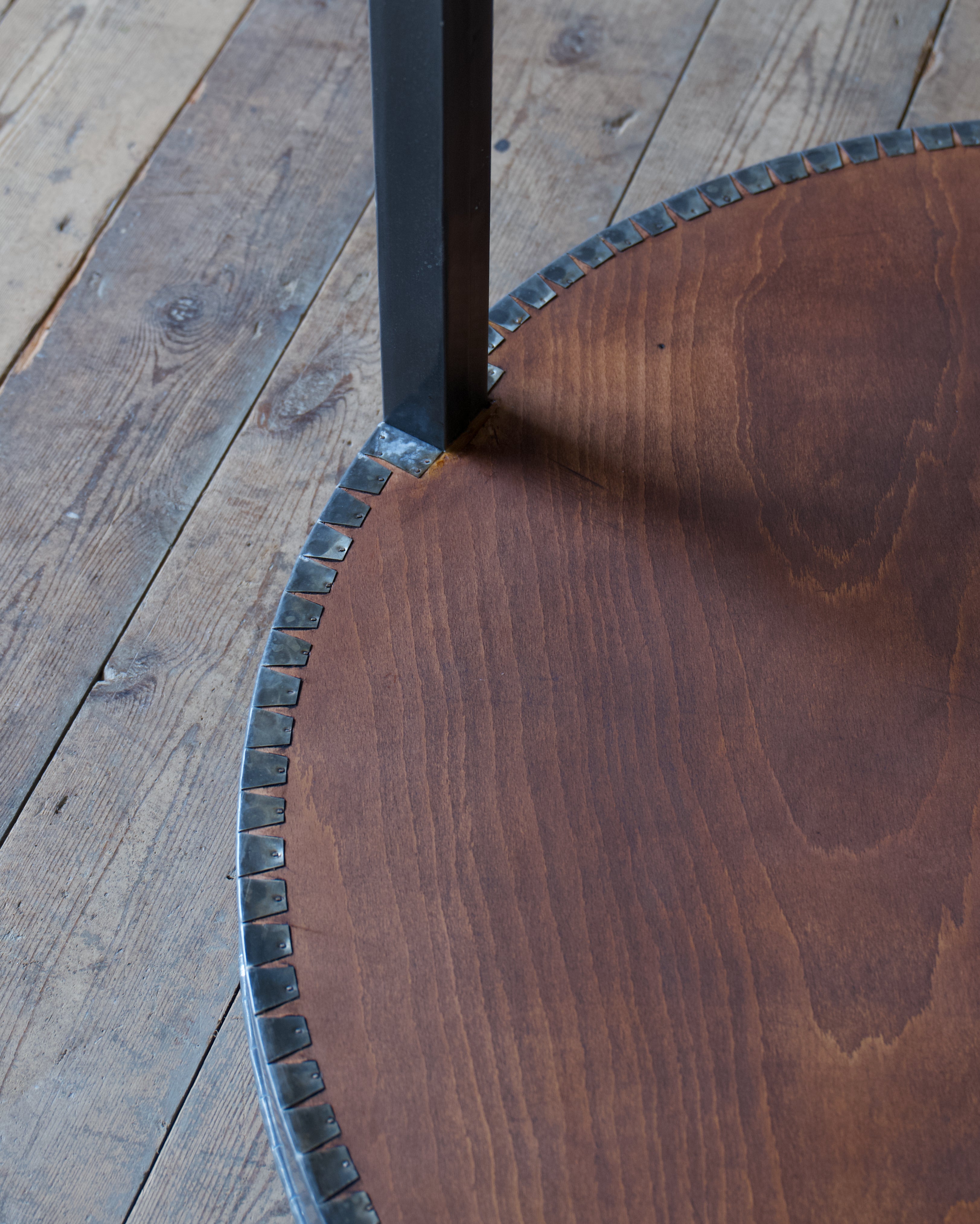 A close up of the underside of a circular table wrapped in zinc, set on a wood floor.