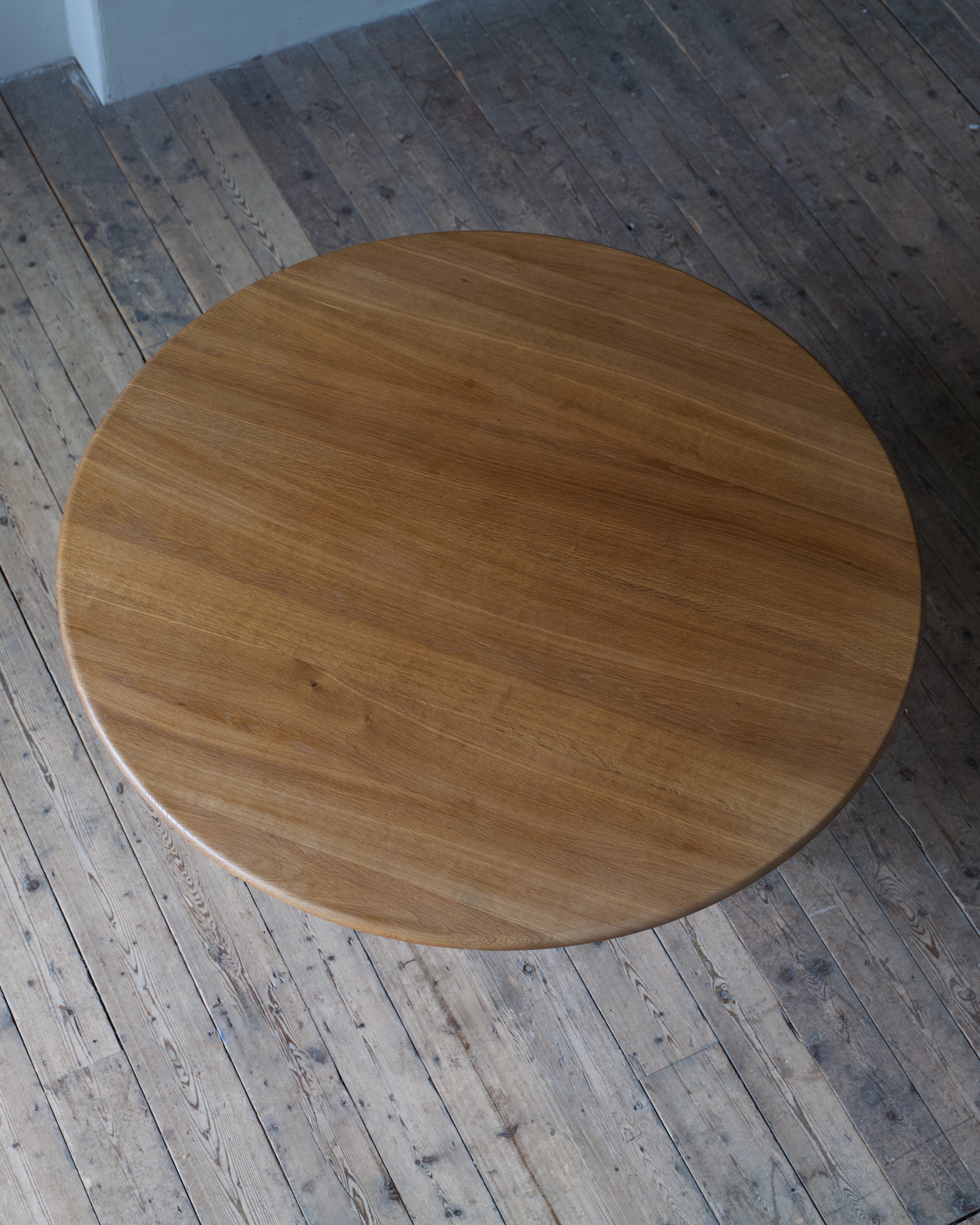 A circular oak table top with a warm medium-brown finish and visible wood grain, photographed from above on a rustic plank floor.
