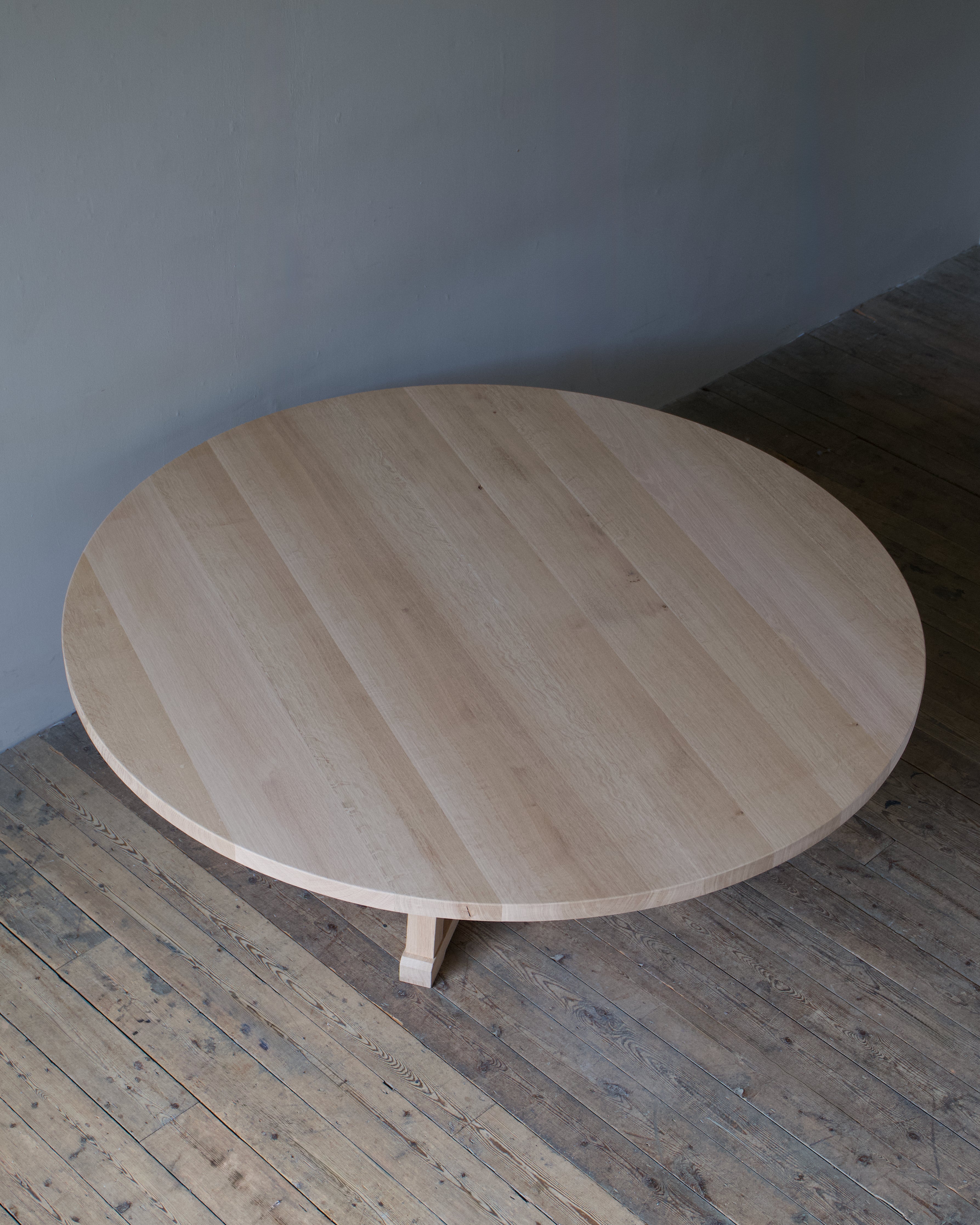 A circular, light oak table viewed from the top in a room with a wooden floor and light grey wall.