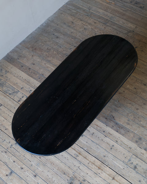 A dark oval wooden table with a glossy black finish, photographed from an overhead angle on a rustic light brown wooden plank floor.