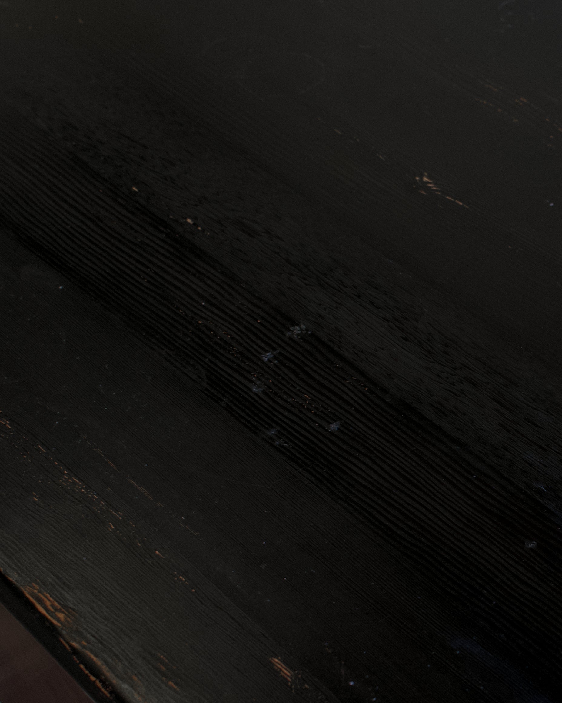 A close-up of a dark, distressed black wood surface with visible grain and subtle wear.