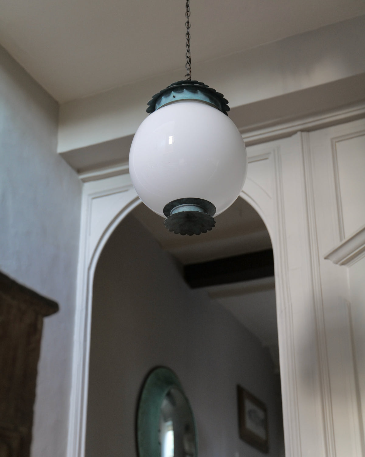 A vintage-style pendant light with a large white glass globe shade and dark brass accents, hanging in a grand doorway.