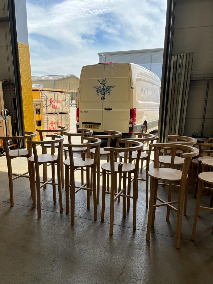 Wooden bar stools in a warehouse with a van in the background