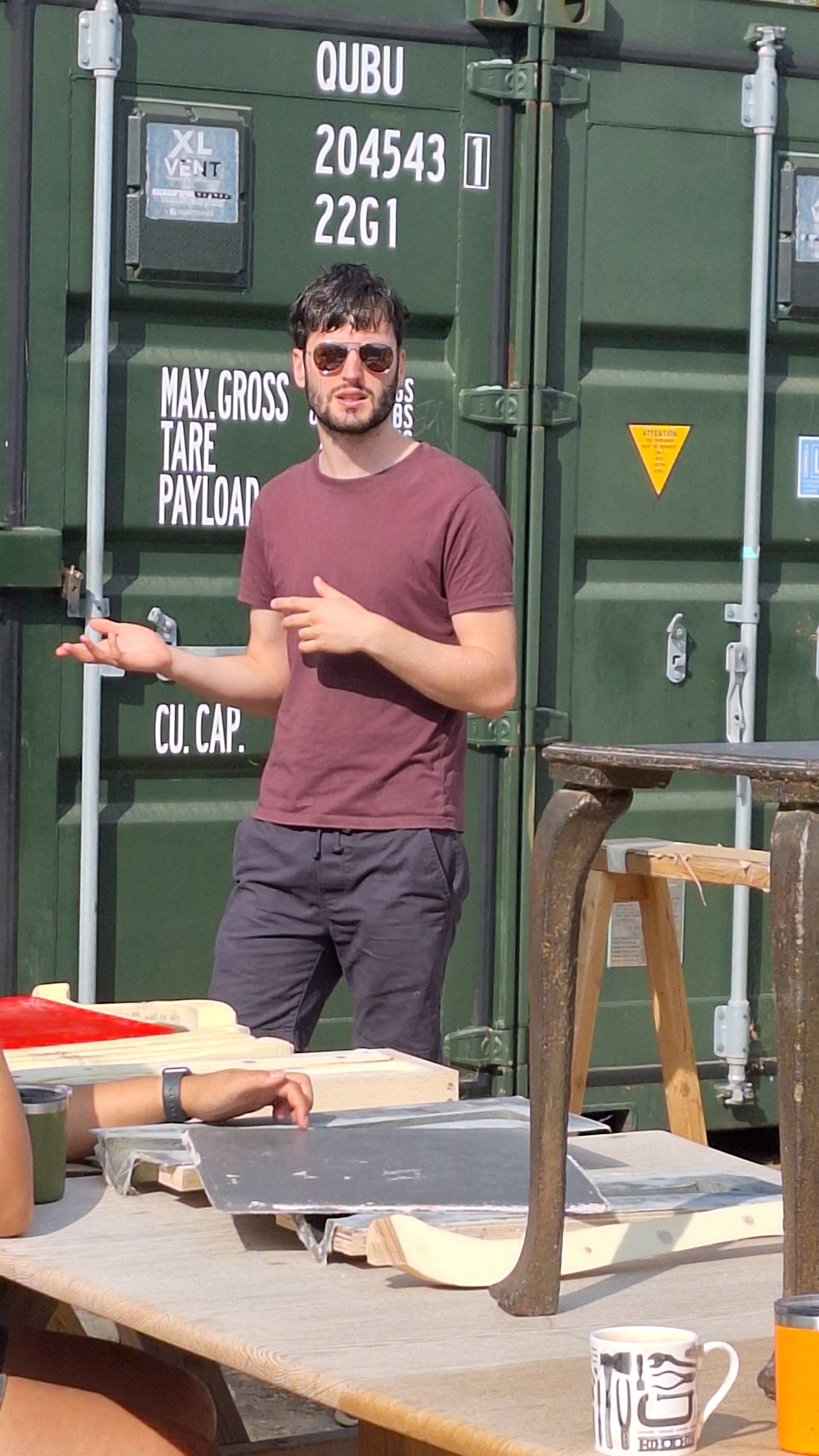 A man talking in front on a shipping container with a cast iron table - the fire table in the foreground