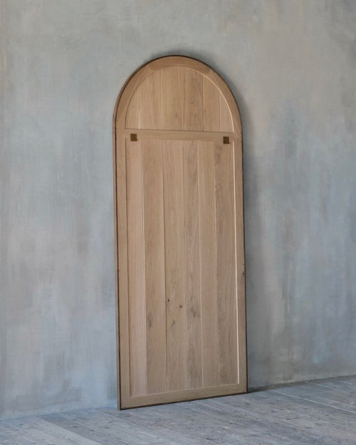 Wooden arched mirror against a plain wall